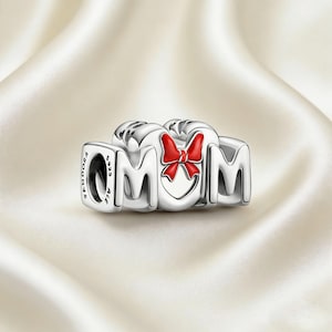 May include: A silver charm with the word "MOM" spelled out in individual letters. The letter "O" features a red bow. The charm is made of silver and has the brand name "PANDORA" engraved on the side.