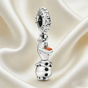 May include: A silver charm depicting Olaf from Disney's Frozen. The charm has a round top with the word "Pandora" and a small gem. Olaf has a carrot nose, black buttons, and a smiling face. The charm is made of sterling silver.