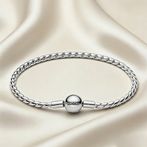 Puede incluir: Una pulsera plateada con un diseño de cadena trenzada. La pulsera presenta un cierre redondo con el nombre de la marca "Pandora" grabado. La pulsera se muestra sobre una superficie de satén blanco.