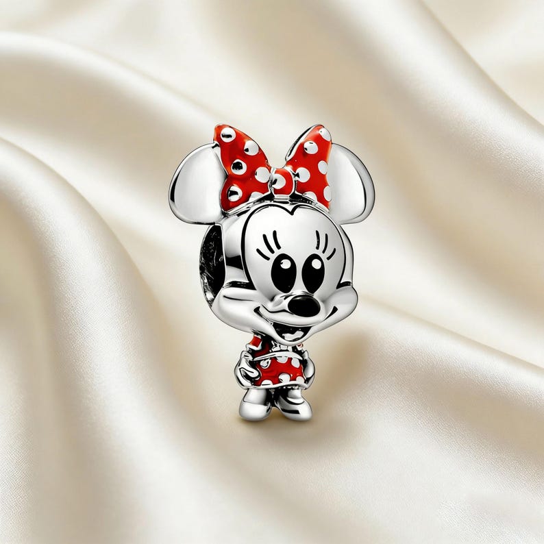 Puede incluir: Un charm de plata con un personaje de dibujos animados con un lazo y un vestido de lunares rojos y blancos. El charm tiene orejas grandes y una cara sonriente. El charm es probablemente de metal y est&aacute; dise&ntilde;ado para una pulsera o collar.