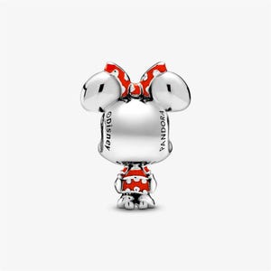 Puede incluir: Un charm plateado con un personaje con orejas grandes, un vestido de lunares rojos y blancos y un lazo rojo. El charm tiene los logotipos de Disney y Pandora.