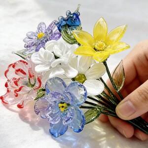 May include: A colorful bouquet of glass flowers, including yellow, white, red, blue, and purple blooms. The flowers are held together by green stems. The bouquet is a decorative item.