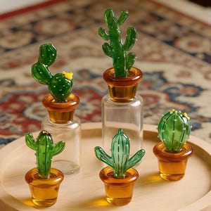 Peut inclure: Une collection de sculptures miniatures de cactus en verre de différentes formes et tailles, chacune placée dans un petit pot ou une bouteille de couleur ambre. Les cactus sont d'un vert vif et l'ensemble repose sur un plateau rond en bois.