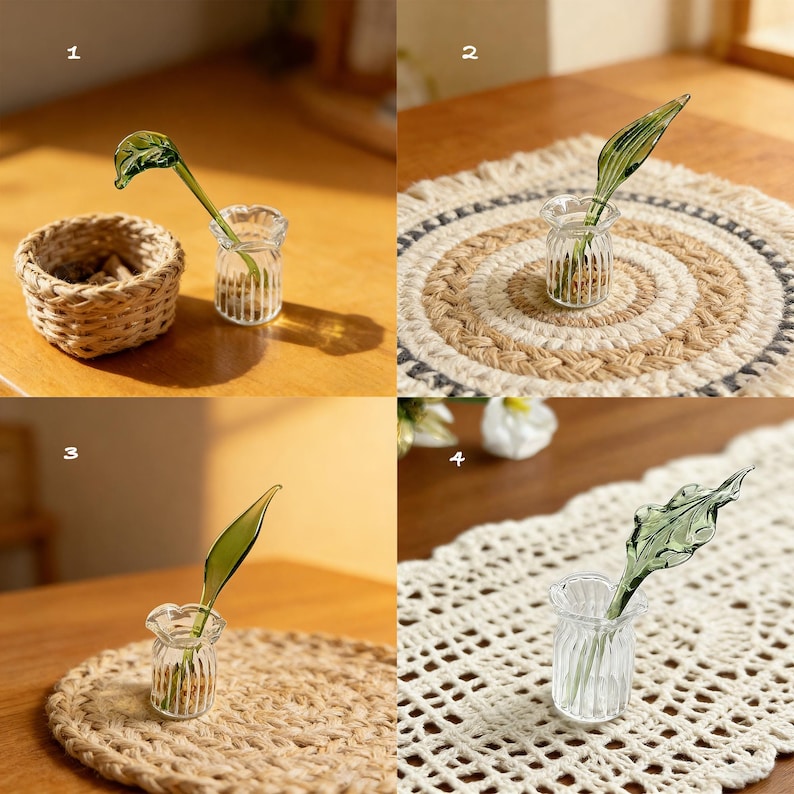 May include: A clear glass bud vase with a green glass leaf stem. The vase is small and ribbed, and the leaf has detailed veining. The vase is displayed on a wooden table with a woven basket and a woven placemat.
