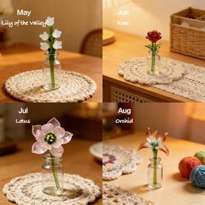 May include: Four glass flower sculptures in small vases, each representing a different month: May (Lily of the Valley), June (Rose), July (Lotus), and August (Orchid). The flowers are in clear glass vases on decorative mats.