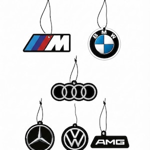 May include: A set of six hanging car air fresheners featuring automotive logos including the BMW M emblem, the BMW roundel, the Audi four-ring logo, the Mercedes-Benz three-pointed star, the Volkswagen logo, and the AMG badge, each with a black string.