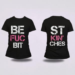 May include: Two black t-shirts with white and pink text. One shirt reads "BE FUC BIT" and the other reads "ST KIN' CHES". The shirts are displayed on a white background.