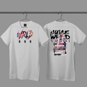 May include: White t-shirt with front and back graphics. The front graphic says "WORLD" in a colorful, graffiti-style font, with the numbers "999" below. The back graphic says "JUICE WRLD" in black, with an image of a person sitting on a stack of cassette tapes.