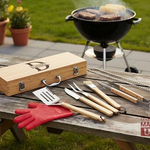 May include: A wooden barbecue tool set in a rectangular case with the name Daniel engraved on the lid. The set includes a metal spatula, fork, knife, brush, and tongs with wooden handles, alongside a red silicone glove on a wooden table.