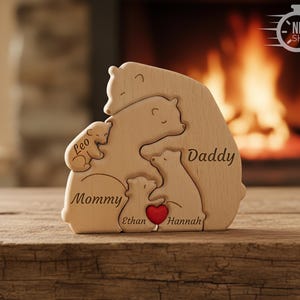 May include: A wooden bear family puzzle with the words "Mommy," "Daddy," and children's names engraved. A red heart is included. The puzzle is made of light-colored wood and is displayed on a wooden surface.