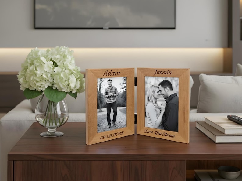 Op de afbeelding: Een houten dubbele fotolijst met twee zwart-witfoto's. Het linkerframe heeft de naam "Adam" en de datum "09.05.2025" gegraveerd. Het rechterframe heeft de naam "Jasmin" en de tekst "Love You Always" gegraveerd.
