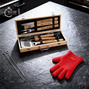 May include: A wooden carrying case containing stainless steel grilling tools with wooden handles engraved with the text KING OF THE GRILL, including a knife, brush, fork, tongs, and spatula, alongside two metal skewers and a red silicone oven mitt.