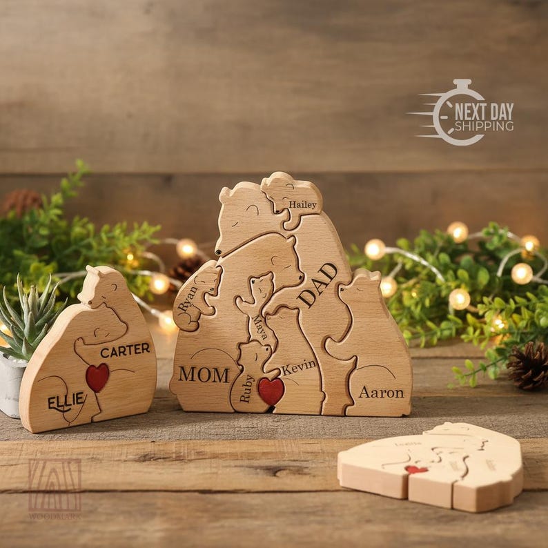 May include: Wooden bear family puzzle with names engraved on each bear. The puzzle features a mom, dad, and children, with a red heart detail. A smaller bear puzzle with a heart is also present. The background includes greenery and fairy lights.