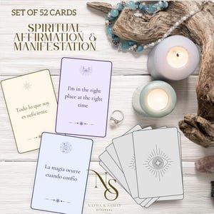 Puede incluir: Un juego de 52 cartas de afirmación con el texto "Spiritual Affirmation & Manifestation". Las cartas tienen varias afirmaciones en inglés y español. La imagen incluye velas encendidas, un anillo y elementos decorativos.