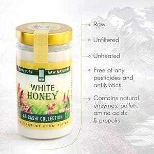 May include: A glass jar of white honey with a gold lid and a yellow label. The label reads "WHITE HONEY" and "AT-BASHI COLLECTION". The text also states the honey is raw, unfiltered, unheated, and free of pesticides and antibiotics.
