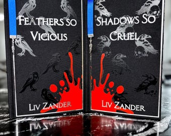 May include: Two hardcover books with black covers and silver lettering. The titles are "Feathers So Vicious" and "Shadows So Cruel" by Liv Zander. The covers feature crow illustrations and red splatter designs. Blue ribbon bookmarks are attached.