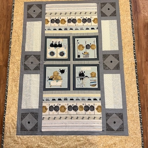 May include: A handmade quilt with a whimsical laundry theme. The quilt features a central panel with illustrated scenes of birds doing laundry, framed by gray and cream patterned borders. The outer border is a light tan with a floral design.