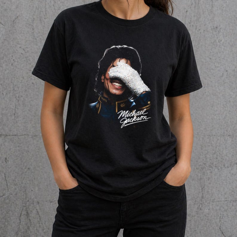 May include: Black t-shirt featuring a smiling image of Michael Jackson, wearing a white glove and a blue jacket. The text "Michael Jackson" is written in cursive below the image. The shirt is made of a soft material.