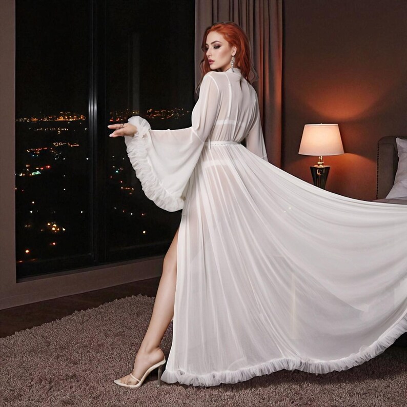 May include: A flowing, white sheer robe with long sleeves and a high slit. The robe features ruffled trim and is worn over a matching lingerie set. The background includes a city skyline at night and a bedroom setting.