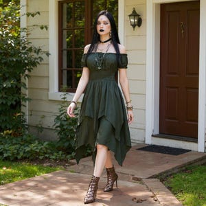 May include: An olive green off-the-shoulder dress with a layered, asymmetrical hemline. The dress is paired with brown lace-up heeled boots. The model is wearing multiple necklaces and bracelets. The background includes a house with a brown door and a window.