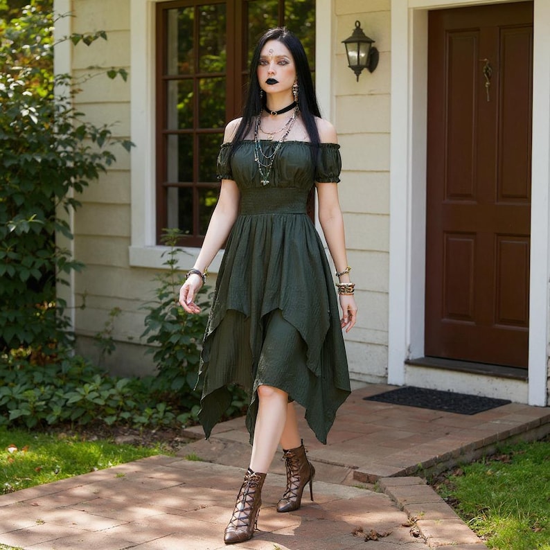 May include: An olive green off-the-shoulder dress with a layered, asymmetrical hemline. The dress is paired with brown lace-up heeled boots. The model is wearing multiple necklaces and bracelets. The background includes a house with a brown door and a window.