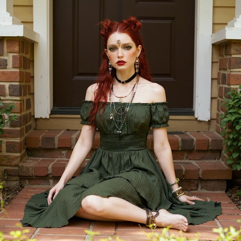 May include: An off-the-shoulder olive green dress with short sleeves and a tiered skirt. The dress is paired with layered necklaces, bracelets, and a black choker. The person has red hair and is sitting on brick steps.