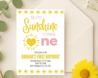 May include: A white invitation card with the text "Our Little Sunshine is turning one" in yellow and pink. The card includes details for Hannah's first birthday, with a yellow sun graphic and a matching envelope.