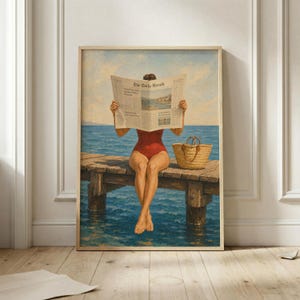May include: A framed wall art print depicting a person in a red swimsuit sitting on a wooden pier over blue water, reading a newspaper titled The Daily Herald. A woven straw tote bag sits on the pier next to the person against a light blue sky.