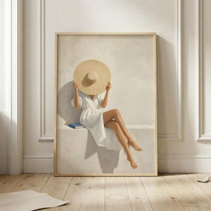 Può includere: Una stampa artistica da parete incorniciata che raffigura una figura con un abito a portafoglio bianco e un grande cappello di paglia beige che ne nasconde il volto. La figura è seduta su una sporgenza con un piccolo libro blu accanto.
