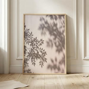 May include: A rectangular wall art print in a light wood frame featuring a soft beige background with the dark brown shadow of tree leaves cast across the surface, creating a layered botanical pattern that fills the entire vertical composition.