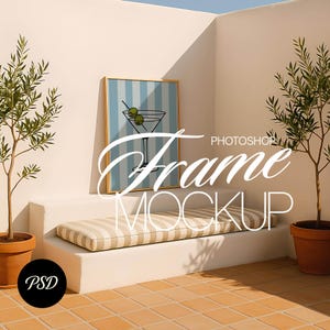 May include: A framed art print featuring a martini glass illustration with olives, set against a blue and white striped background. The frame is gold-colored. The image is displayed on a white step with a striped cushion, flanked by potted plants.