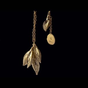 May include: A gold necklace with a cluster of leaves pendant and a smaller leaf charm with a circular tag that reads "H 185".