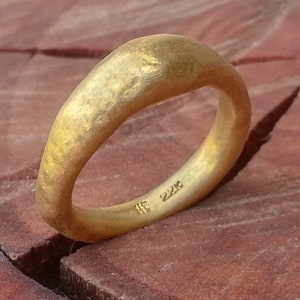 May include: A gold ring with a textured, hammered finish. The ring is wide and has a rounded, slightly curved shape. The inside of the ring is stamped with the number "22K".