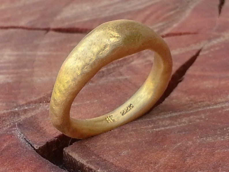 May include: A gold ring with a textured, hammered finish. The ring is wide and has a rounded, slightly curved shape. The inside of the ring is stamped with the number "22K".