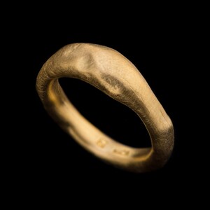 May include: A gold ring with a textured, irregular surface. The ring is thick and has a rounded shape.