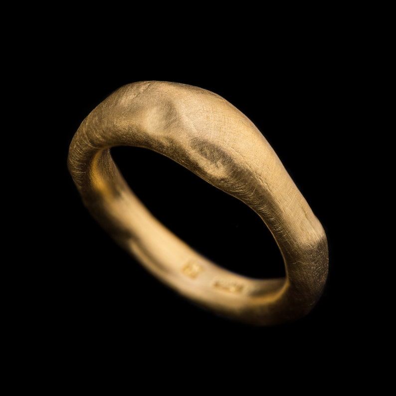 May include: A gold ring with a textured, irregular surface. The ring is thick and has a rounded shape.