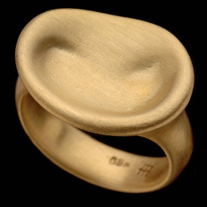 Puede incluir: Un anillo de oro con una parte superior ovalada, lisa y redondeada. El anillo est&aacute; hecho de metal cepillado y tiene un acabado mate.