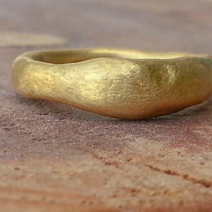 May include: A simple gold band ring with a hammered finish. The ring is made of a smooth, rounded metal and has a slightly irregular shape.