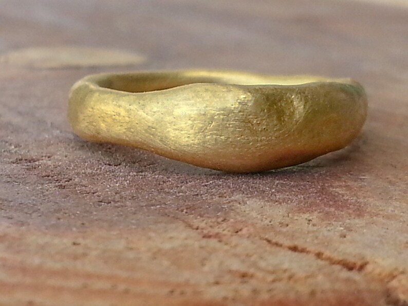 May include: A simple gold band ring with a hammered finish. The ring is made of a smooth, rounded metal and has a slightly irregular shape.