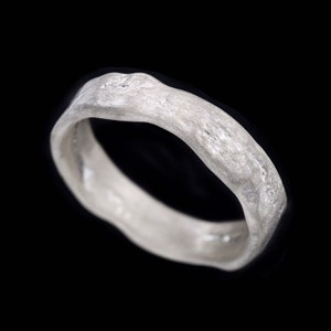 May include: A silver ring with a textured, organic shape. The ring is made of metal and has a smooth, polished finish.