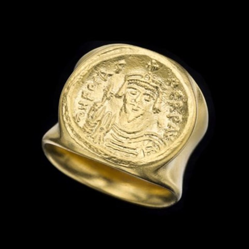 May include: A gold ring with a raised coin-shaped design featuring a profile of a person with a crown and the inscription "CHPEKA".