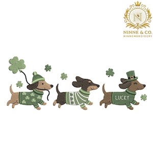 May include: Embroidered design featuring three dachshunds in green sweaters and hats, celebrating St. Patrick's Day. One dog holds a shamrock balloon, another wears a striped sweater, and the last has a top hat with the word "LUCKY".
