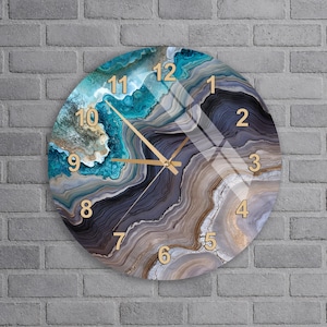 May include: A circular wall clock featuring a printed agate stone pattern in shades of teal, dark blue, grey, and beige. The clock face displays gold-colored Arabic numerals from 1 to 12 and matching gold-colored hour, minute, and second hands.