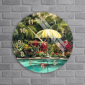 Puede incluir: Un reloj de pared redondo con una escena impresa de una piscina rodeada de exuberantes plantas tropicales y una sombrilla de playa a rayas amarillas y blancas. La esfera tiene números grandes de color claro y manecillas de metal dorado.