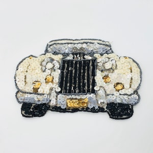 May include: A white, silver, and black beaded car applique. The car is made of sequins and beads and has a detailed front grill.