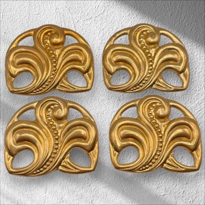 May include: Four gold-colored metal decorative pieces with a swirling, floral design. Each piece has a rounded, slightly curved shape.