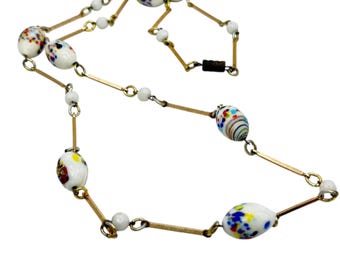 May include: A vintage necklace with white, oval beads adorned with colourful speckled patterns. The necklace features gold-toned metal bars and small white beads. A magnetic clasp secures the necklace. The necklace is a unique piece of jewellery.