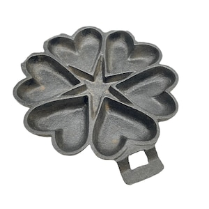 May include: A cast iron heart-shaped waffle maker with a star in the center. The waffle maker has a handle on the bottom.