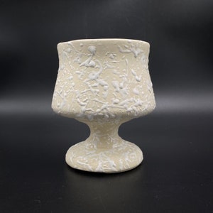May include: A white ceramic planter with a textured, splatter-like design. The planter has a wide, flared top and a pedestal base.