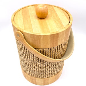 May include: A wooden ice bucket with a woven wicker design and a wooden lid with a knob. The bucket has a brown leather handle.